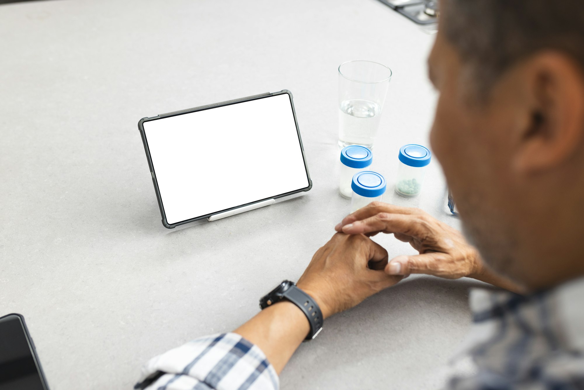 A senior man is seated at a table with medication and a digital tablet, with copy space