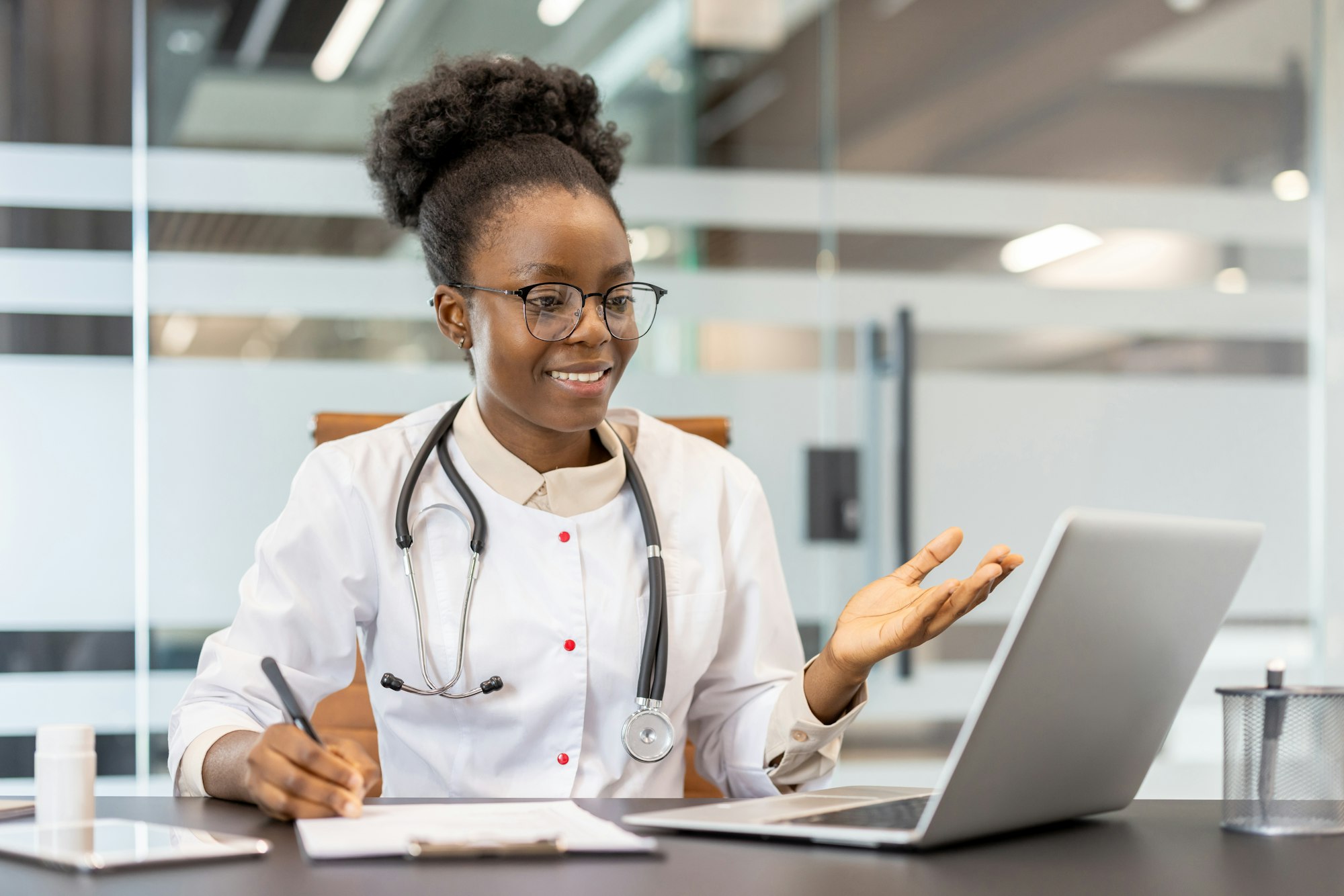 Doctor conducting virtual consultation via video call in modern office with laptop and stethoscope